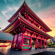 a red Japanese temple with city in the background and sunset sky