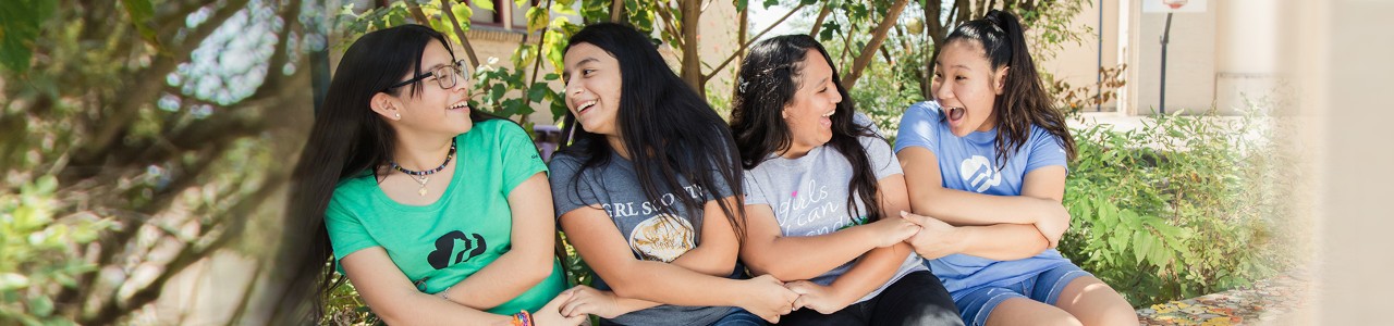  group of high school girl scouts holding hands outside in a seated friendship circle smiling and laughing 