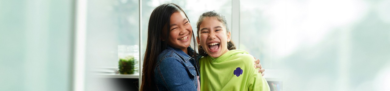  two girls wearing girl scout hoodie and jean jacket hugging and laughing 