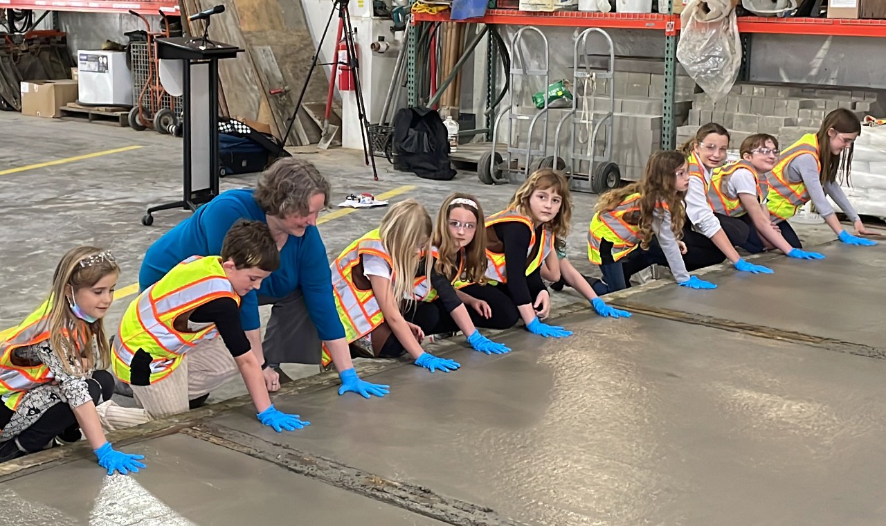 troop of girl scouts wearing high vis vests making handprints in concrete